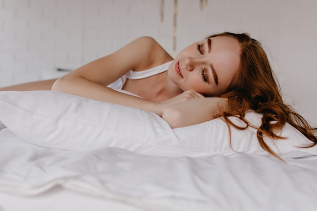 Pleased beautiful woman with trendy makeup sleeping with smile. Indoor photo of enchanting curly girl.
