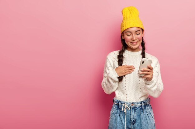 Pleased brunette Korean woman using mobile phone on pink background