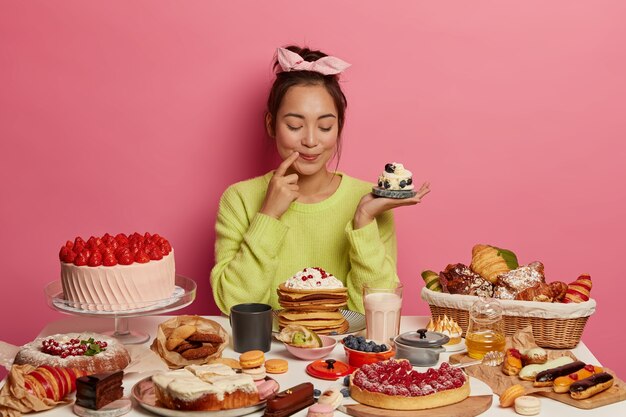 Pleased brunette woman holds small creamy muffin, bakes many desserts for New Year holiday or festive time, demonstrates her culinary abilities