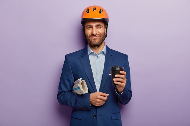 Free photo pleased businessman posing in classy suit and red helmet at the office