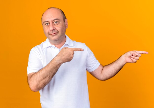 Pleased casual mature man points at side isolated on yellow backgound with copy space