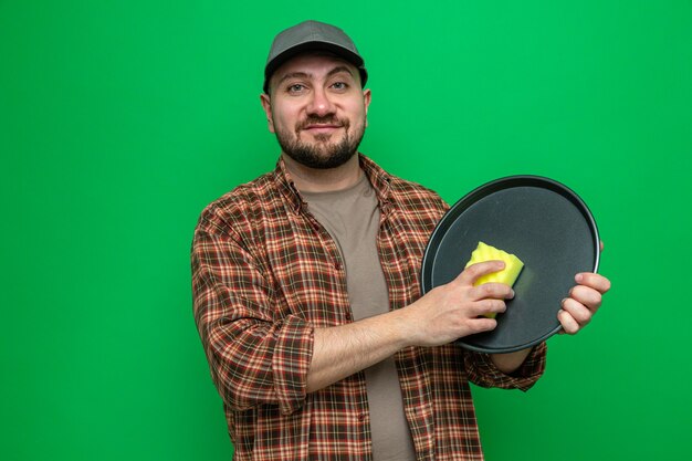 Pleased cleaner man cleaning dishes with sponge 