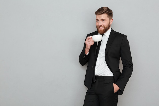 Pleased cool bearded man in suit drinking tea