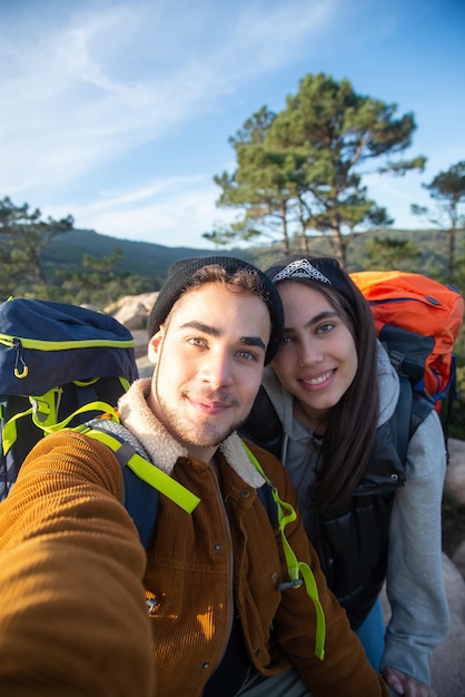 Pleased couple of hikers taking selfie. Man and woman in casual clothes and with backpacks looking at camera. Love, leisure, technology concept