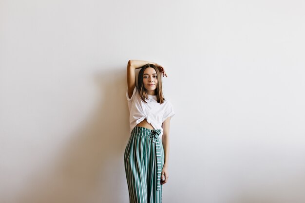 Pleased dark-haired girl in trendy pants posing in her apartment. caucasian fascinating woman isolated.