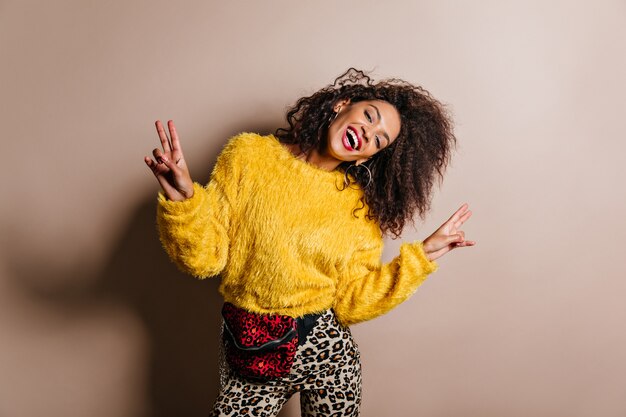 Pleased dark-haired woman in yellow sweater dancing and laughing