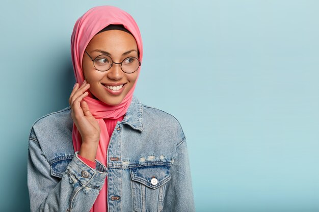 Pleased dark skinned lady has Islamic views, wears transparent glasses