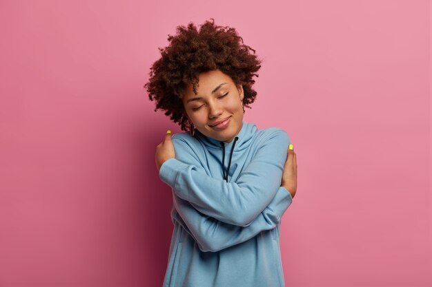 pleased dark skinned woman with afro hair, embraces herself