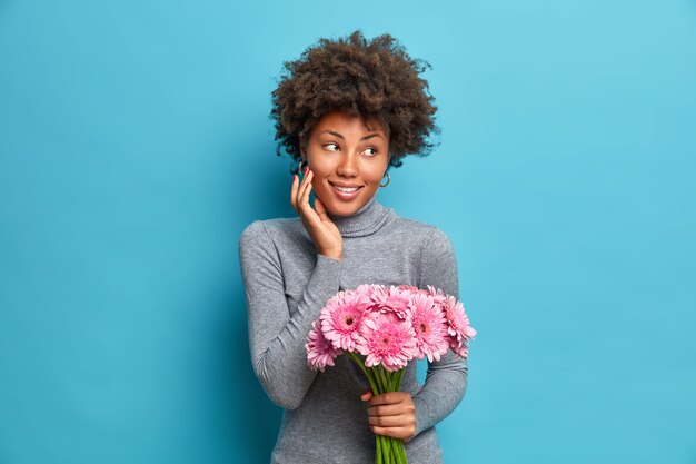 喜んで喜んでアフリカ系アメリカ人の女性がピンクのガーベラの花束を持っています