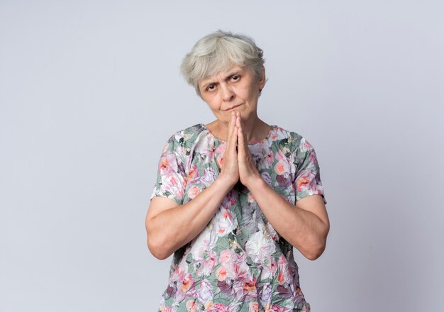 Pleased elderly woman holds hands together isolated on white wall