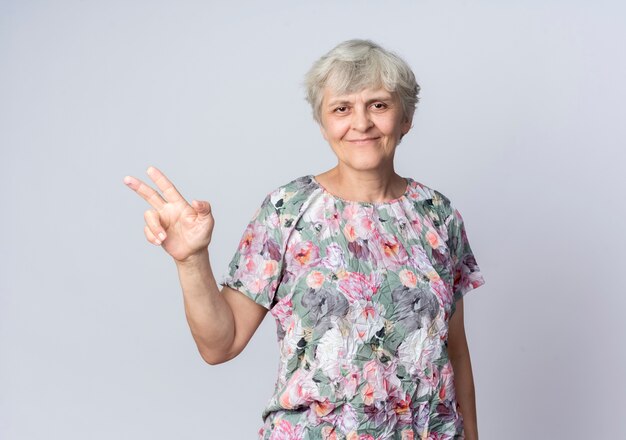 Pleased elderly woman points at side with hand isolated on white wall