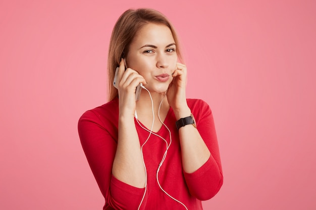 Pleased female enjoys favourite track in earphones