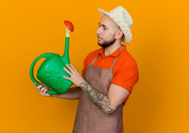 Free photo pleased gardener man wearing gardening hat holds and looks at watering can