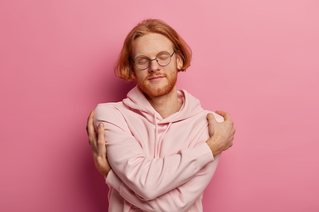 Free photo pleased ginger man keeps arms around his shoulders