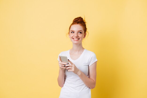 スマートフォンを手で保持しているtシャツで満足している生姜の女性