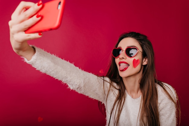 Free photo pleased girl in funny heart glasses taking picture of herself