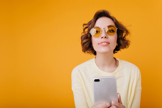 Pleased girl with wavy hairstyle making selfie on orange space