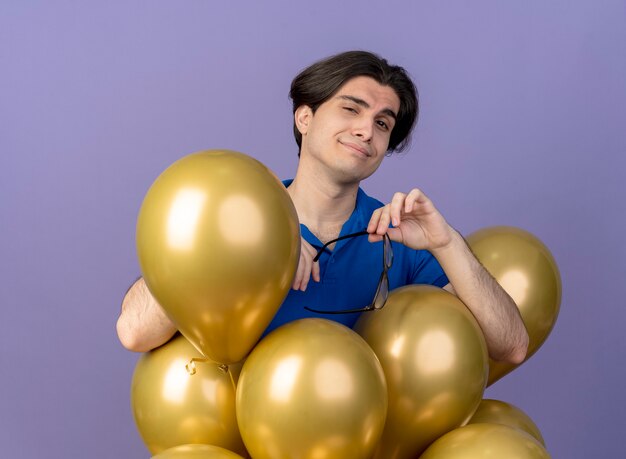 Pleased handsome caucasian man stands with helium balloons holding optical glasses 