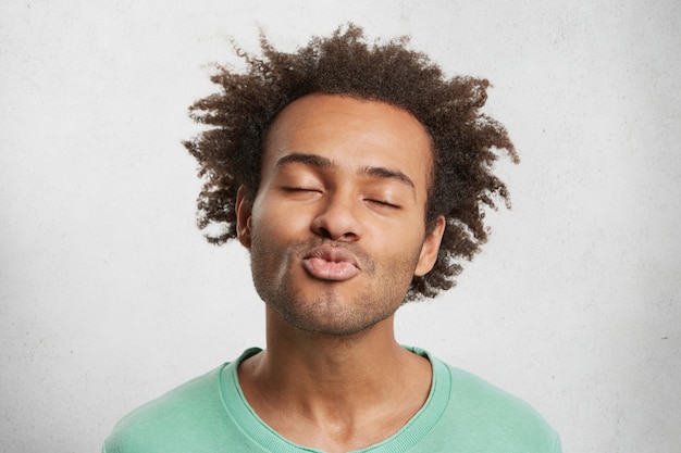 Free photo pleased handsome guy closes eyes with enjoyment, rounds or pouts lips as waits for kiss from girlfriend