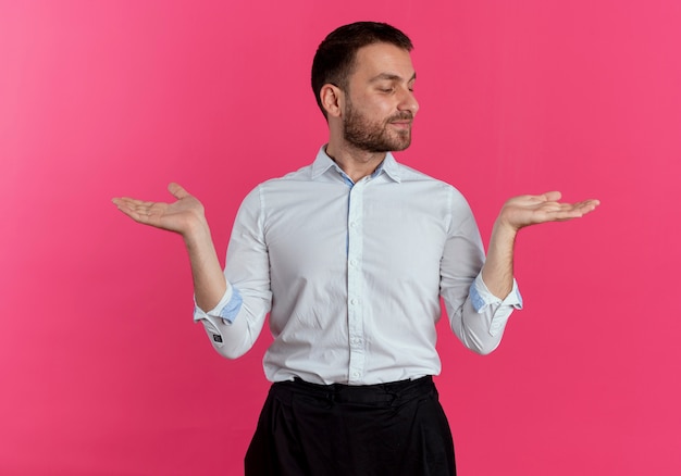 Pleased handsome man holds hands open isolated on pink wall