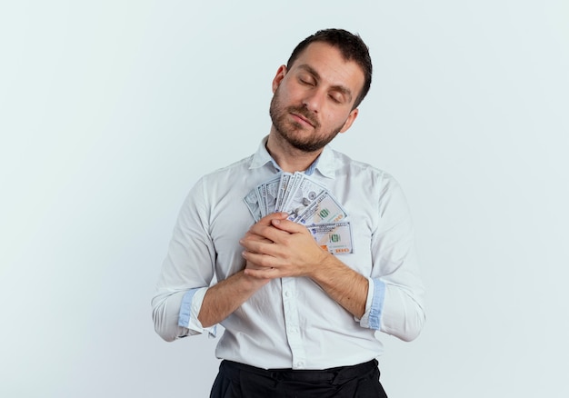 Pleased handsome man holds money with closed eyes isolated on white wall