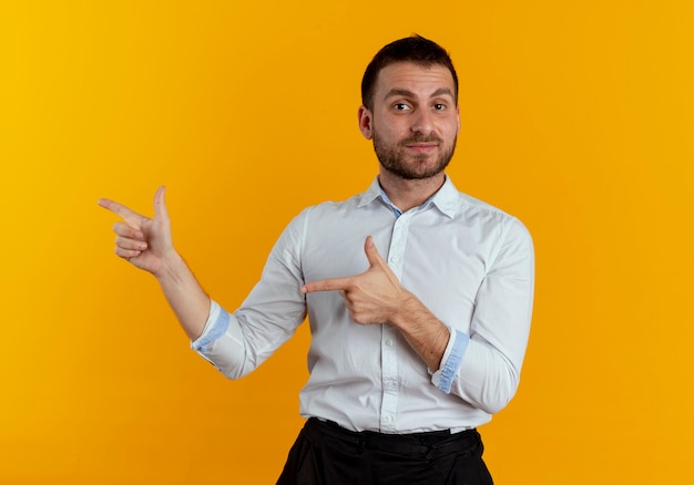 Pleased handsome man points at side with two hands isolated on orange wall