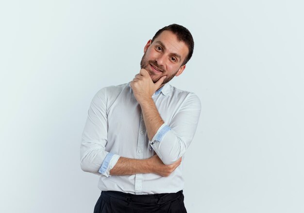 Pleased handsome man puts hand on chin isolated on white wall