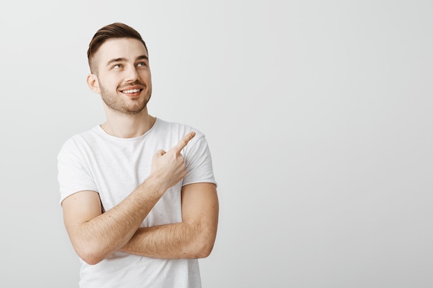 Pleased handsome young man in white t-shirt pointing finger upper right corner