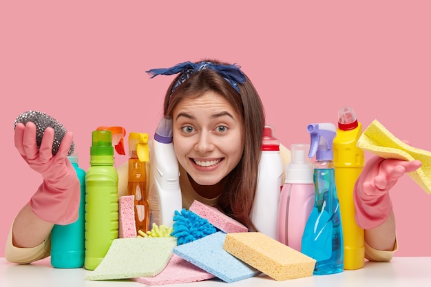 Pleased lady with European appearance, toothy smile wears headband, looks positively through detergents