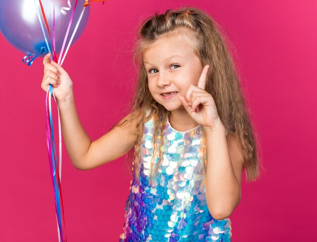 헬륨 풍선을 들고 복사 공간이 분홍색 벽에 고립 가리키는 기쁘게 작은 금발 소녀