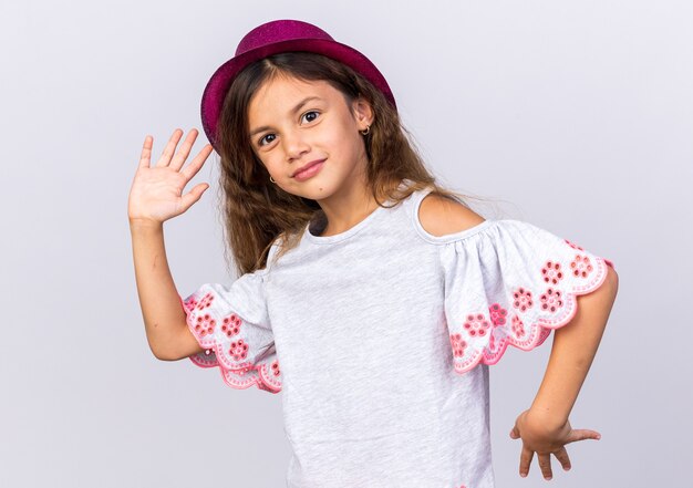 Contenta piccola ragazza caucasica con cappello da festa viola che tiene le mani aperte isolate sul muro bianco con spazio di copia