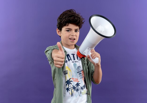 Pleased little schoolboy holding loudspeaker his thumb up isolated on purple wall