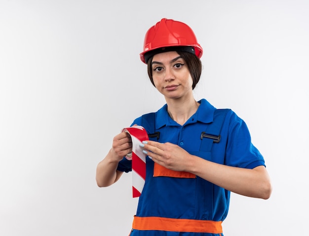 Pleased looking at camera young builder woman in uniform holding duct tape 