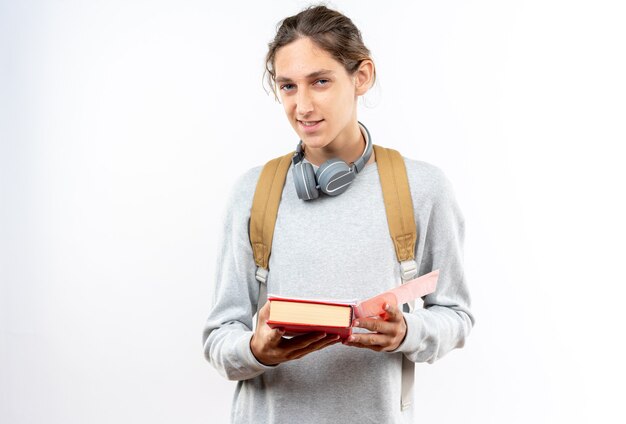 本を持っている首にヘッドフォン付きのバックパックを身に着けているカメラの若い男の学生を見て喜んで