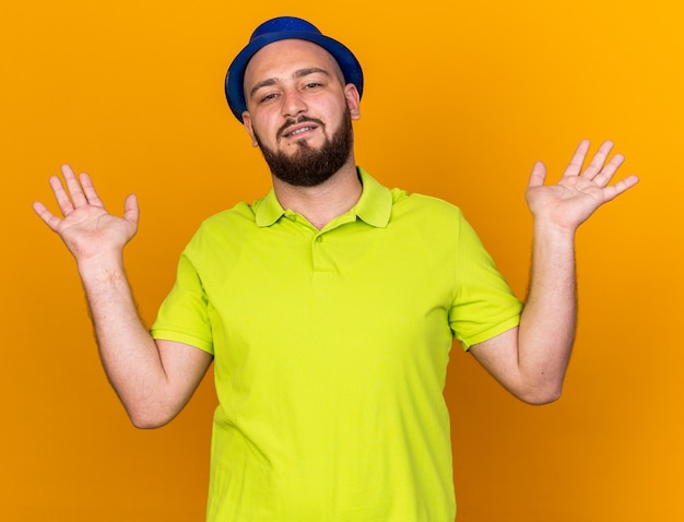 Pleased looking camera young man wearing party hat spreading hands 