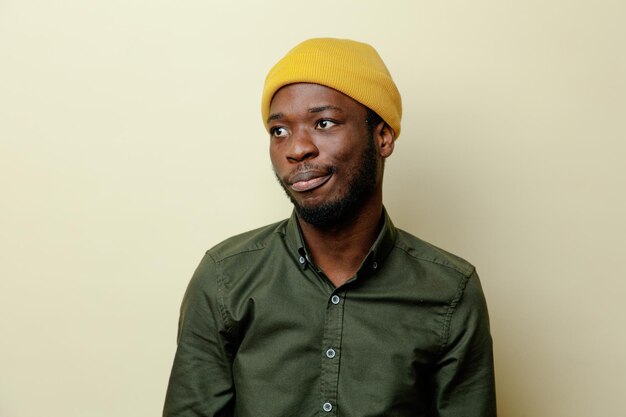 Pleased looking at side young african american male in hat wearing green shirt isoloated on white background