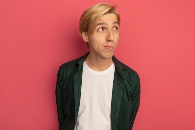 Free photo pleased looking at side young blonde guy wearing green t-shirt holding hand on waist