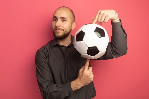 Pleased looking straight ahead young handsome guy holding ball on fingers isolated on pink