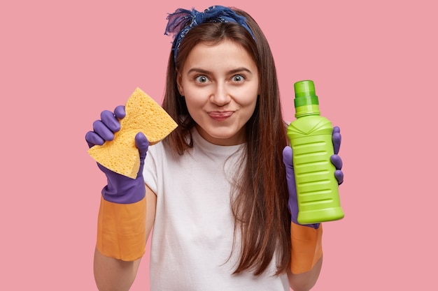 Pleased lovely woman holds cleaning set for different services, dressed in speacial uniform