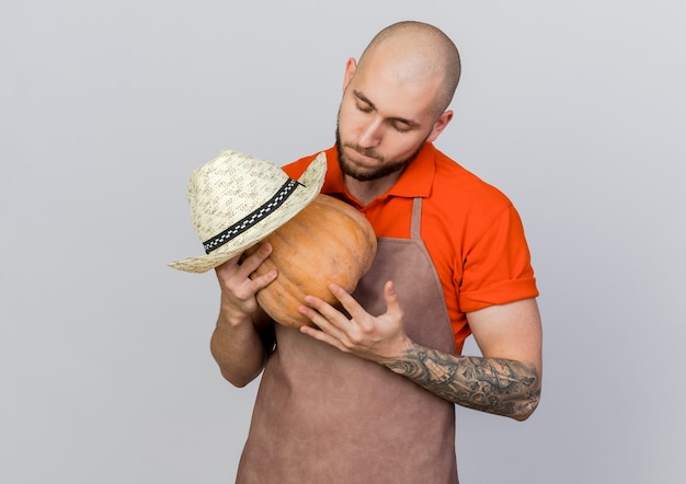 Free photo pleased male gardener looks at pumpkin wearing gardening hat