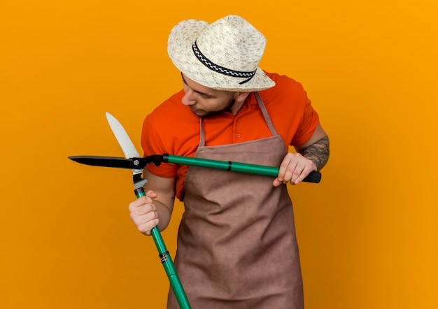 Il giardiniere maschio soddisfatto che indossa il cappello da giardinaggio tiene e guarda i tagliaunghie da giardino