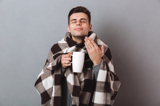 Pleased man in warm plaid holding hot tea smells it.