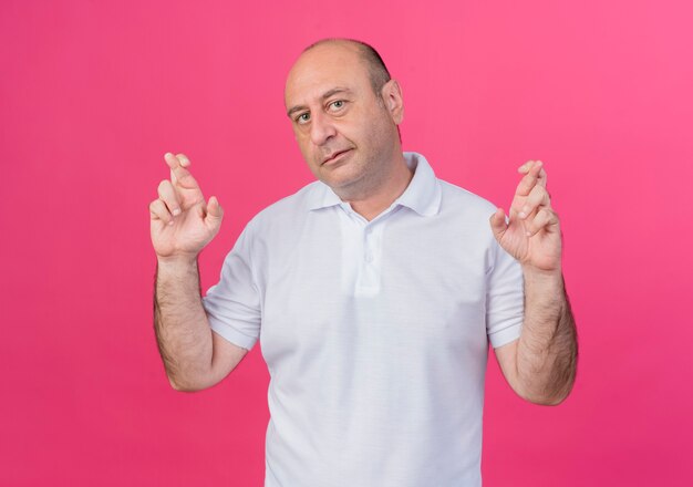 pleased mature businessman looking at front and doing crossed fingers gesture