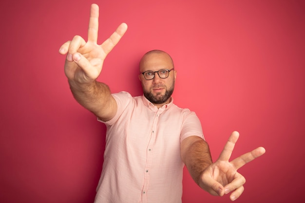 Foto gratuita felice uomo calvo di mezza età che indossa la maglietta rosa con gli occhiali che mostra gesto di pace isolato sul rosa