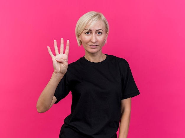 Довольная белокурая славянская женщина средних лет, смотрящая вперед, показывает четыре руки, изолированные на розовой стене с копией пространства