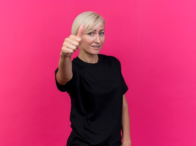 Pleased middle-aged blonde slavic woman  showing thumb up isolated on crimson wall with copy space