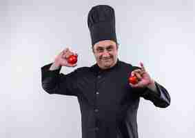 Free photo pleased middle-aged male cook in chef uniform holding domates in both hands on isolated white wall