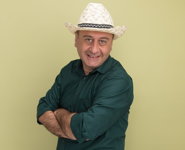 Free Photo pleased middle-aged man wearing green t-shirt and hat crossing hands isolated on olive green wall