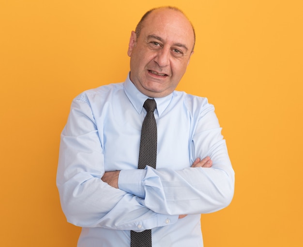 Pleased middle-aged man wearing white t-shirt with tie crossing hands isolated on orange wall