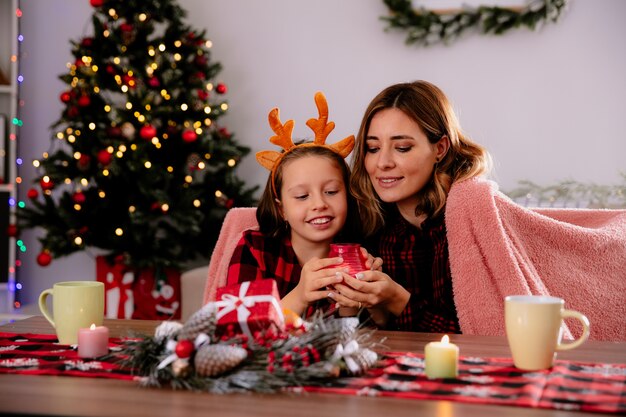 家でクリスマスの時間を楽しんでいるテーブルに座ってろうそくを手に持って見て喜ぶ母と娘